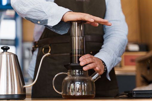 Aeropress coffee close-up: barista press to device and coffee drops pours trought aeropress to pot. Alternative scandinavian coffee brewing method.