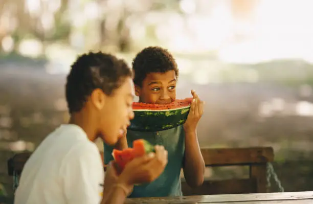 Side image of two young men are sitting and eating watermelons