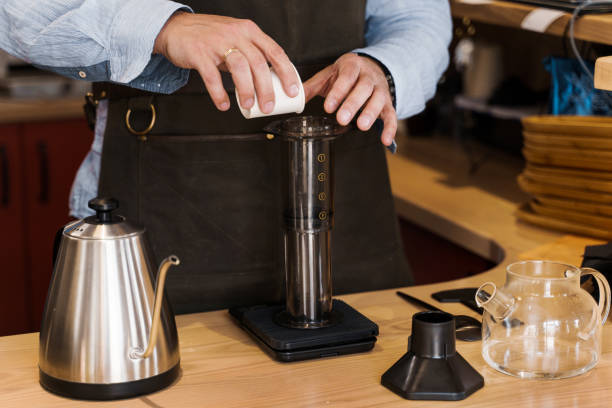 istock Aeropress coffee: barista spread ground coffee to pot. Alternative coffee brewing method. Handsome bearded barista makes tasty Scandinavian coffee 1253672102
