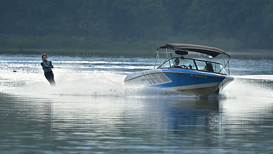 Highly skilled female water skier on Bantam Lake in Connecticut, towed by a turning speedboat with a female driver and passenger