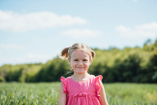 A portrait of a young girl standing in an agricultural field, looking at the camera and smiling.