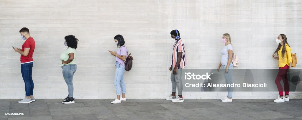 Young people from different cultures and race waiting in queue outside shop market while keeping social distance - Corona virus spread prevention concept Waiting In Line Stock Photo