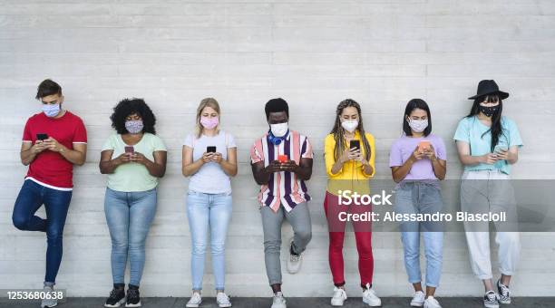 Young People Wearing Face Mask Using Mobile Smartphone Outdoor Multiracial Friends Having Fun With New Technology Social Media App During Corona Virus Outbreak Youth Millennial Lifestyle Concept Stock Photo - Download Image Now