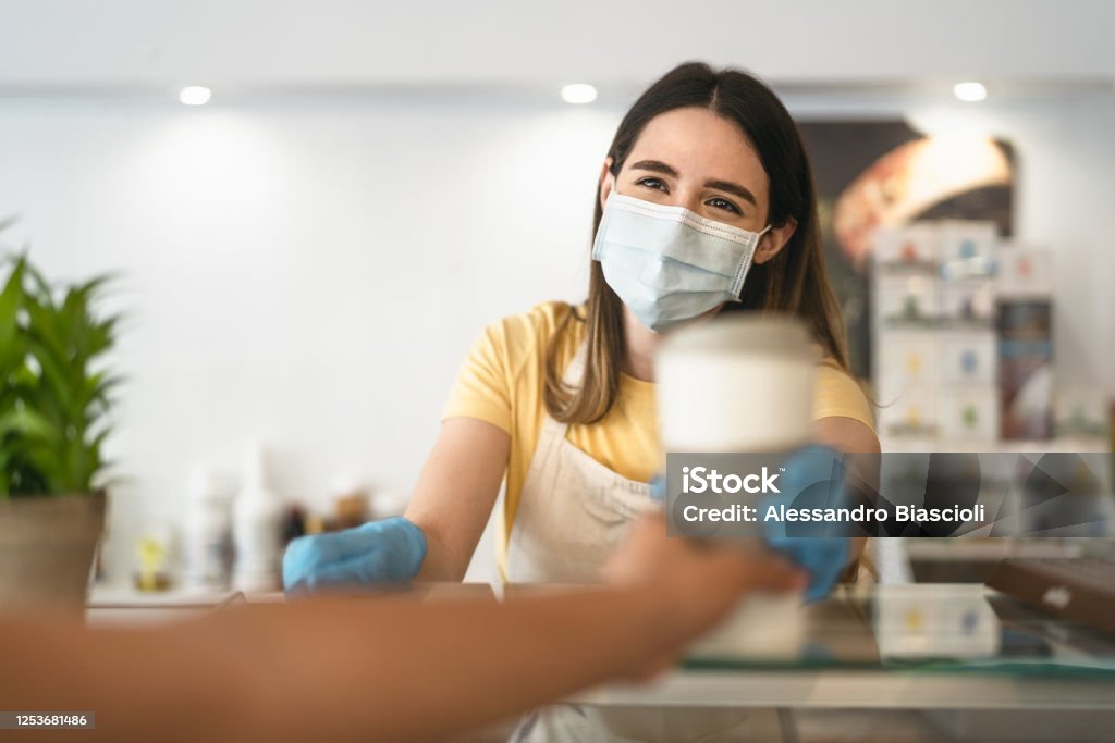 Bar owner working only with take away orders during corona virus outbreak - Young woman worker wearing face surgical mask giving coffee to customer - Healthcare and drinks concept Protective Face Mask Stock Photo