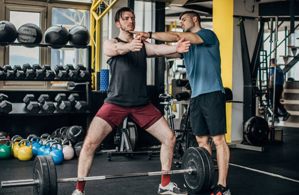 istock Young man training with weights in the gym with personal trainer 1253681719