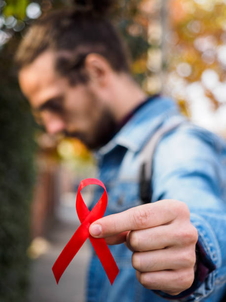 bir adam elinde, aids ve hiv ile mücadelesi simgeleyen kırmızı bir kurdele tutar. aids'e karşı dünya savaşı günü. bürokrasi yakın çekim, kopyalama alanı. kavram: hiv ve aids için bir test almak - world aids day stok fotoğraflar ve resimler