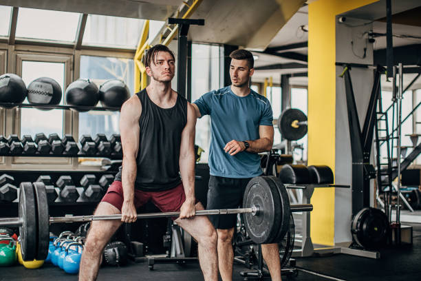 istock Man lifting weights in the gym with personal trainer 1253685731