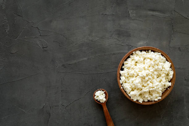 istock Cottage cheese in wooden bowl on white table top view copy space 1253687467