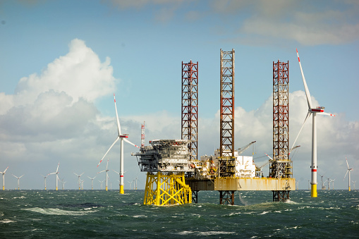 Vista épica de grandes aerogeneradores offshore de 8MW, parque eólico en el horizonte en el mar del norte con barco jack up y plataforma offshore en mar ondulado photo