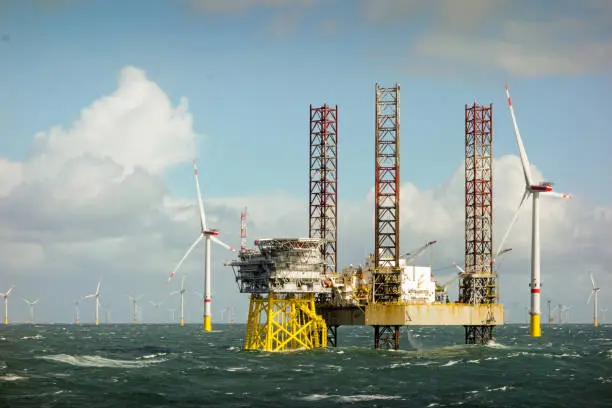 Photo of Epic view on Large offshore 8MW wind turbines, wind farm on the horizont in north sea with jack up boat and offshore platform in wavy sea