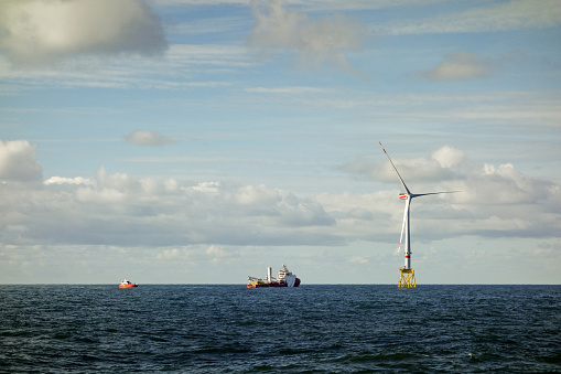 Large offshore 8MW wind turbines, transfer vessel and rescue boat - jetty on the horizont in north sea with dramatic sky.