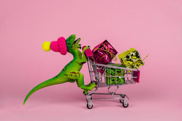 istock funny plastic toy dinosaur wearing tiny knitted hat and driving shopping trolley 1253691606
