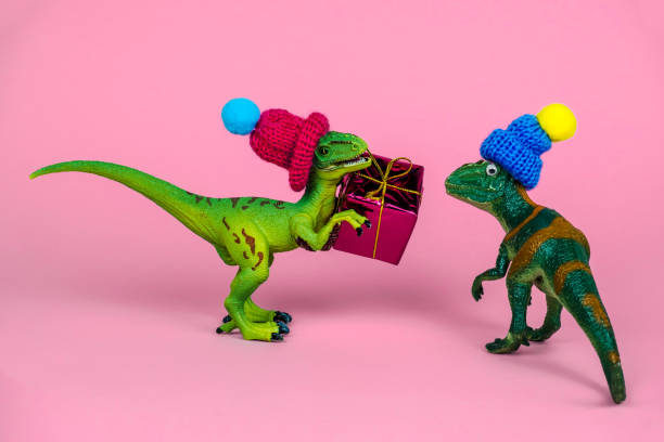 istock cute green plastic toy dinosaur wearing knitted hat and holding present box 1253691644
