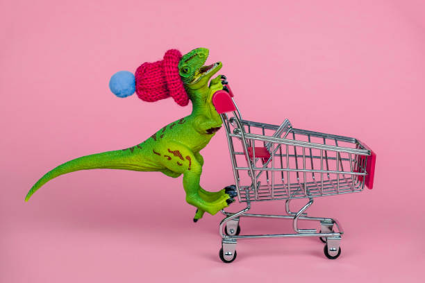 istock funny plastic toy dinosaur wearing tiny knitted hat and driving shopping trolley 1253691745