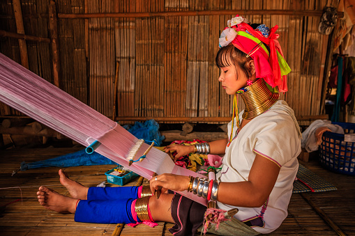 Long-neck woman from Padaung (Karen) tribe weaving on a loom, Mae Hong Son Province in Northern Thailand.