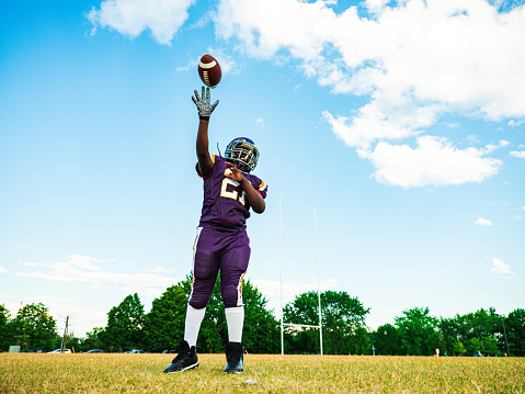 African American Junior Football player getting during game practice at the outdoor field. He is throwing a ball in the air.