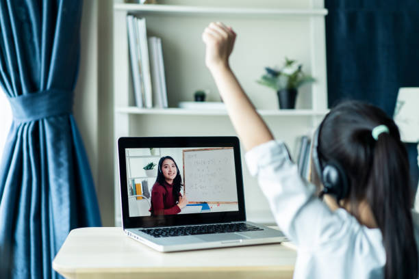 istock Homeschool Asian little young girl student learning virtual internet online class from school teacher by remote meeting due to covid pandemic. Female teaching math by using headphone and whiteboard. 1253698896