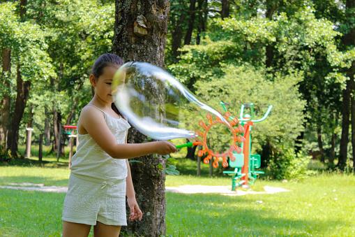 A girl in nature, she makes big soap bubbles. Bubble Activities. Girl is playing with big bubbles outdoor. Active summer leisure for kids