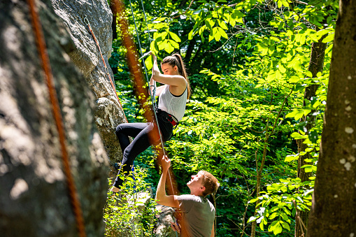 Caucasian female athlete climbing on the rock mountain. Young male helping her with holding the climbing rope.