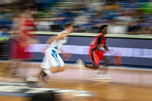 Blurred motion of basketball players playing match in court.