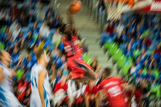 Blurred motion of basketball player in red jersey slam dunking ball during the match.