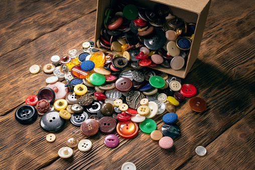 Heap of colorful retro buttons in the cardboard box on the wooden table background.