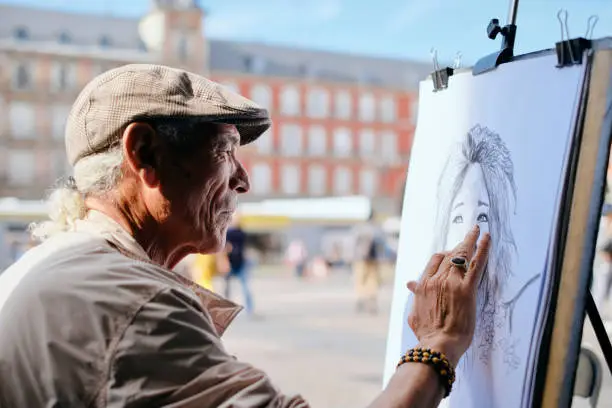 Photo of Old Male Street Painter Drawing Portrait Of Tourist