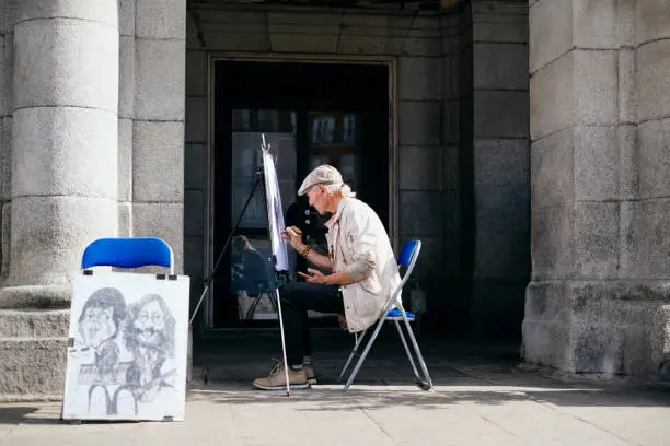 Photo of Old Male Street Painter Drawing Portrait Of Tourist