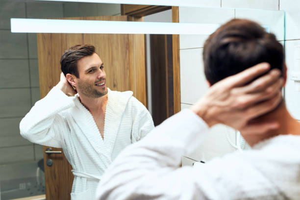 istock Happy man in a bathrobe looking him self in a mirror. 1253712528