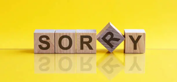 Photo of SORRY the word is written on a wooden block. The image is mirrored in the glossy surface. For your design, the concept is front view.