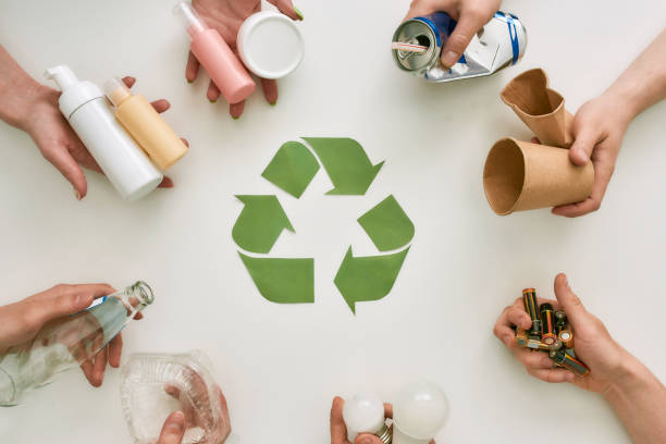 Your life improved. Top view of many hands holding different waste, garbage types with recycling sign made of paper in the center over white background Top view of many hands holding different waste, garbage types with recycling sign made of paper in the center over white background. Sorting, recycling waste concept. Horizontal shot. Top view garbage dump stock pictures, royalty-free photos & images