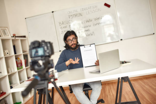 istock Python course online. Young caucasian man teacher in glasses looking at webcam and giving online class while sitting at his workplace at home 1253720420