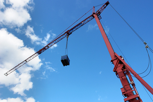 Red construction crane. Box dangling. Blue sky.