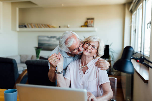 Happy elderly couple having fun at home Cheerful senior lovers sitting at home, using a laptop, having coffee, kissing and enjoying themselves video chat kisses stock pictures, royalty-free photos & images