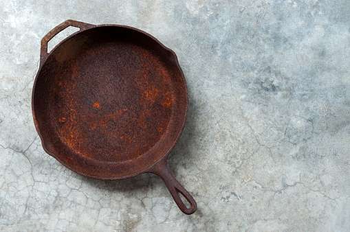 Old rusty round cast iron frying pan on   grey cement background, view from above