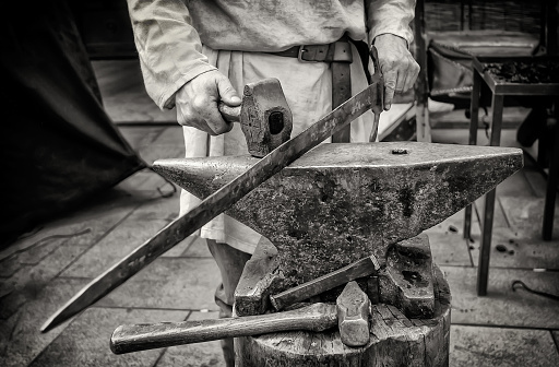 craftsman forging a sword with a hammer blow black and white