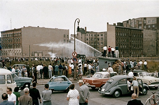 Checkpoint Charlie, Berlin (West), 1961. Ten days after East Berlin was closed (Soviet zone) to the West,  angry West Berliner tried to hinder the construction of the Berlin Wall. They are prevented by water cannons from the East Berlin border troops. Refugees were shot. Furthermore: spectators, parked cars, border facilities and buildings.