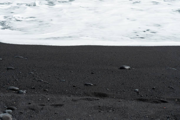 istock Oceanic wave with white foam rolls over black sand beach with pebble . Silky black beach texture. Minimalistic black background. Tenerife voulcanic sandy shore. 1253738452
