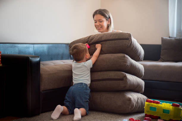 mother playing hide and seek with her toddler son, hidding behind pile of sofa cushions - hidding imagens e fotografias de stock