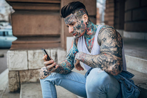 istock Modern man with whole body covered in tattoos using phone outdoors on steps 1253752801