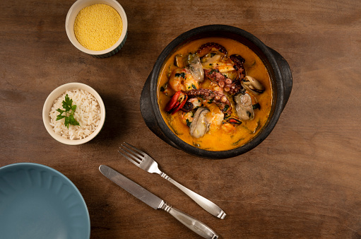 Hand made clay pan with the Brazilian dish named Moqueca, along with a side of rice and farofa