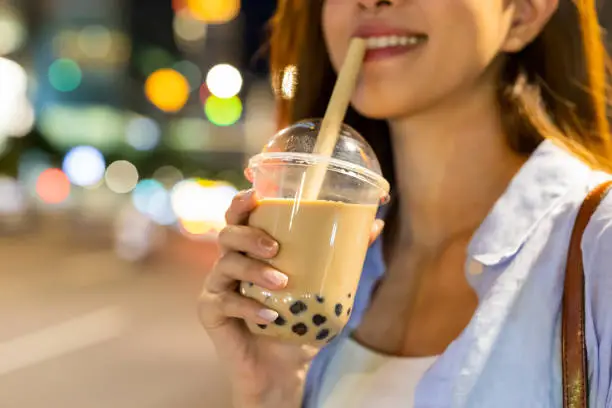 asian woman is holding bubble pearl milk tea outdoor in the evening