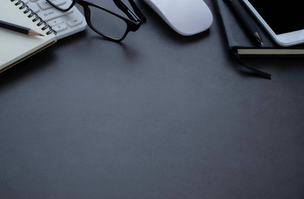 istock Dark grey office desk table with keyboard, notebook and glasses, mouse with equipment other office supplies. Business and finance concept. Workplace, Flat lay with blank copy space, top view. 1253779957