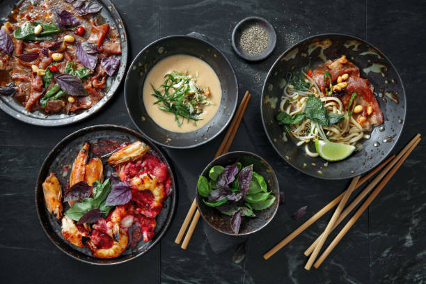 Traditional Asian Dishes for Family Dinner. Soup with Crab and Authentic Pho Beef Noodle Soup. Japanese Wagyu Beef Tataki. Grilled Tiger Prawns. Flat lay top-down composition on black background asian food stock pictures, royalty-free photos & images