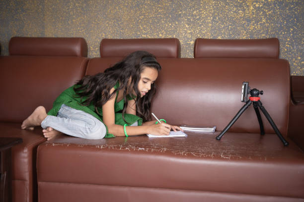 concept of improper, lazy and way of studying during homeschooling or e-learning and make kids sleepy or boredom, young girl busy in writing by looking into mobile on sofa during covid-19 pandemic - homework teenager mobile phone school imagens e fotografias de stock