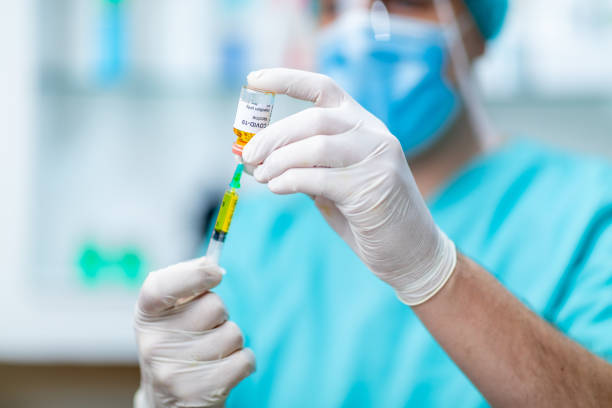 istock Doctor's hands in surgical gloves pulling COVID-19 vaccine liquid from vial 1253804873