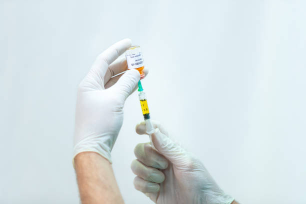 istock Hands in surgical gloves pulling COVID-19 vaccine liquid from vial 1253804902