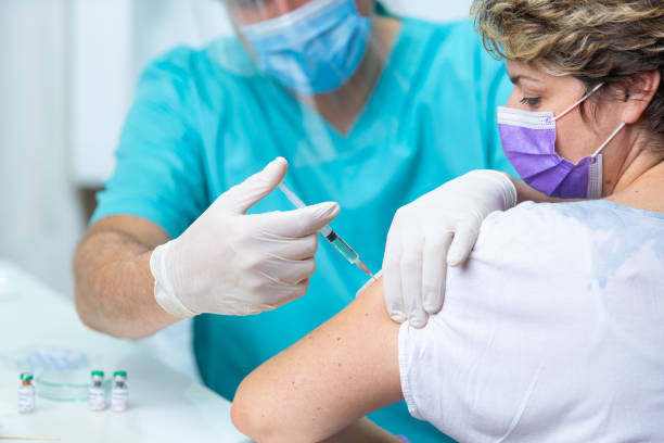 paciente do sexo feminino com máscara facial olhando para o braço enquanto recebe vacina contra gripe - syringe vaccination human hand medical procedure - fotografias e filmes do acervo