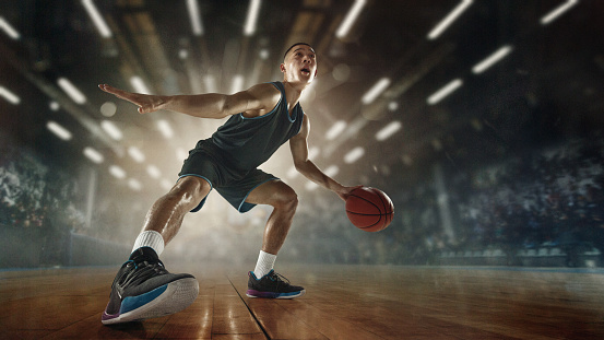 Step. Young male basketball player with ball scoring a goal at the stadium lighted with flashlights. Looks expressive and excitable. Concept of sport, movement, energy and dynamic, healthy lifestyle.