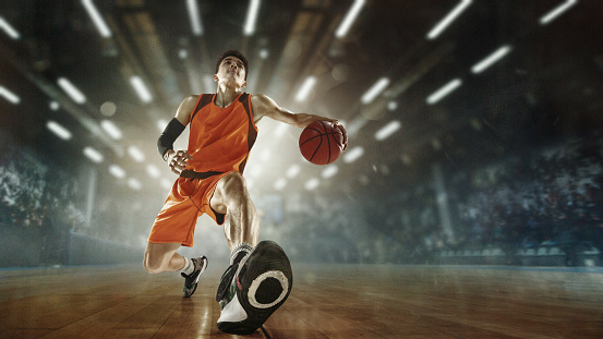 Action. Young male basketball player with ball scoring a goal at the stadium lighted with flashlights. Looks expressive and excitable. Concept of sport, movement, energy and dynamic, healthy lifestyle.
